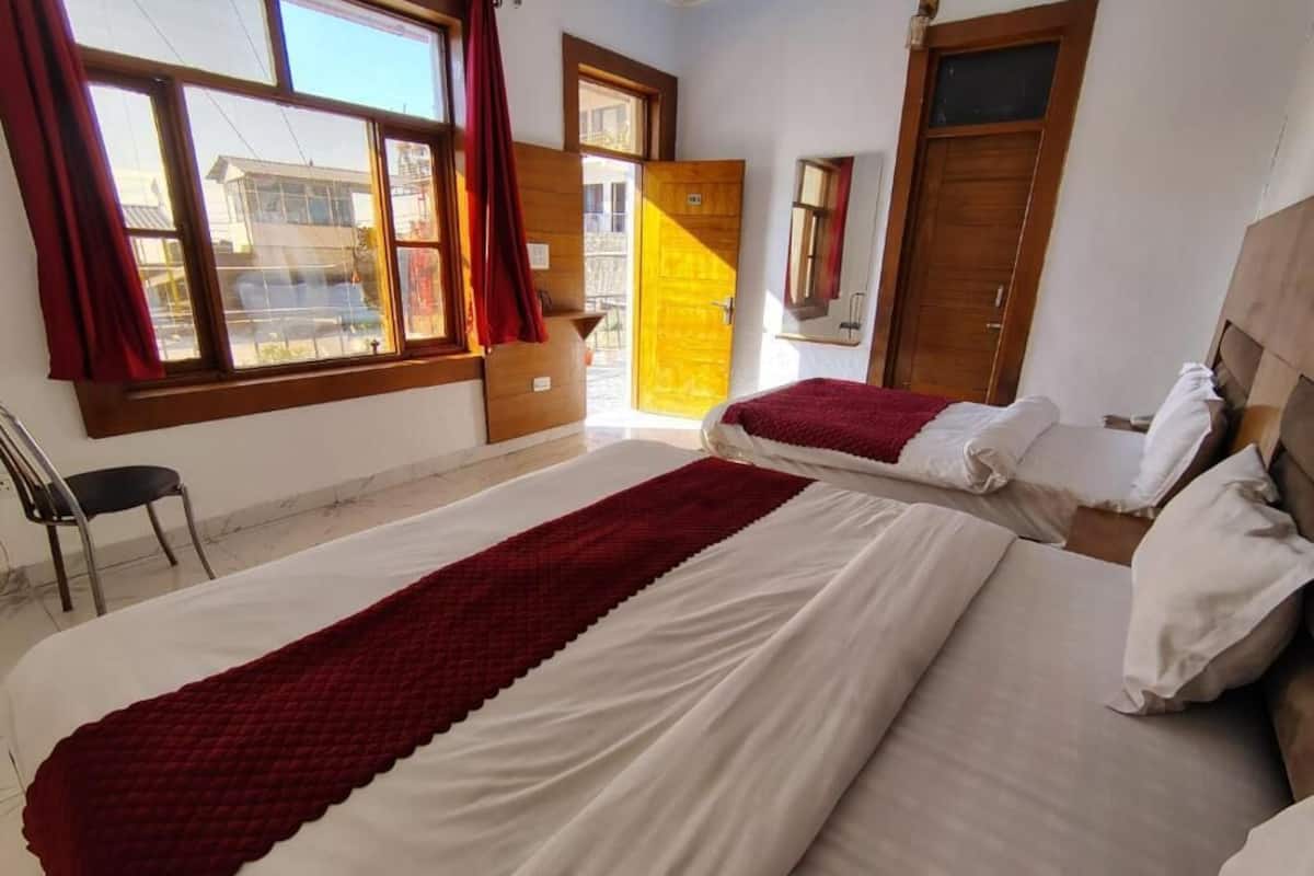Ein Hotelzimmer mit zwei Betten, einem Holzschrank, einem Spiegel und einem Fenster mit Vorhängen.