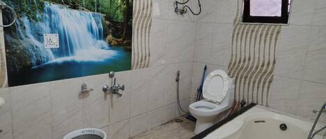 A bathroom with a waterfall mural, a bathtub, a toilet, and a trash can.