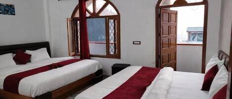 A hotel room with two beds, a wooden headboard, a window with a view, and a red curtain.