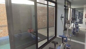 Un gimnasio con equipo de ejercicio, ventanas amplias y una pared de ladrillo visible desde el exterior.