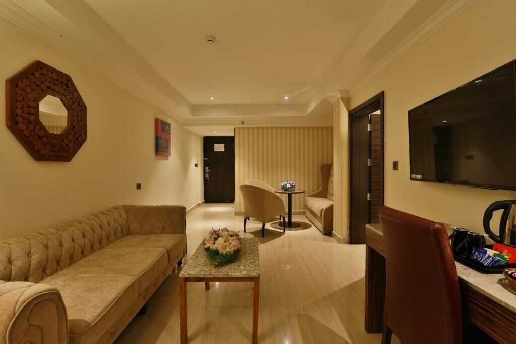 A hotel room with a sofa, a small table with a flower arrangement, a chair, a TV, and a minibar.