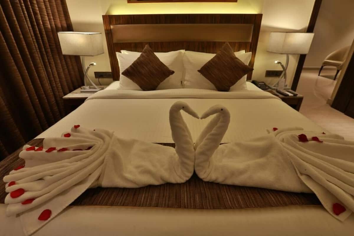 A hotel room with a neatly made bed, two pillows, a nightstand with a lamp, and a chair.