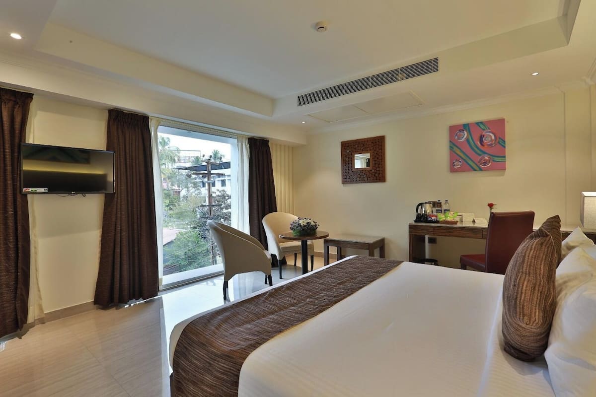 A hotel room with a large bed, a desk with a chair, a TV, and a window with curtains.