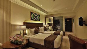 Una camera d'albergo con due letti, una scrivania, una sedia, una lampada e un vaso con fiori decorativi.
