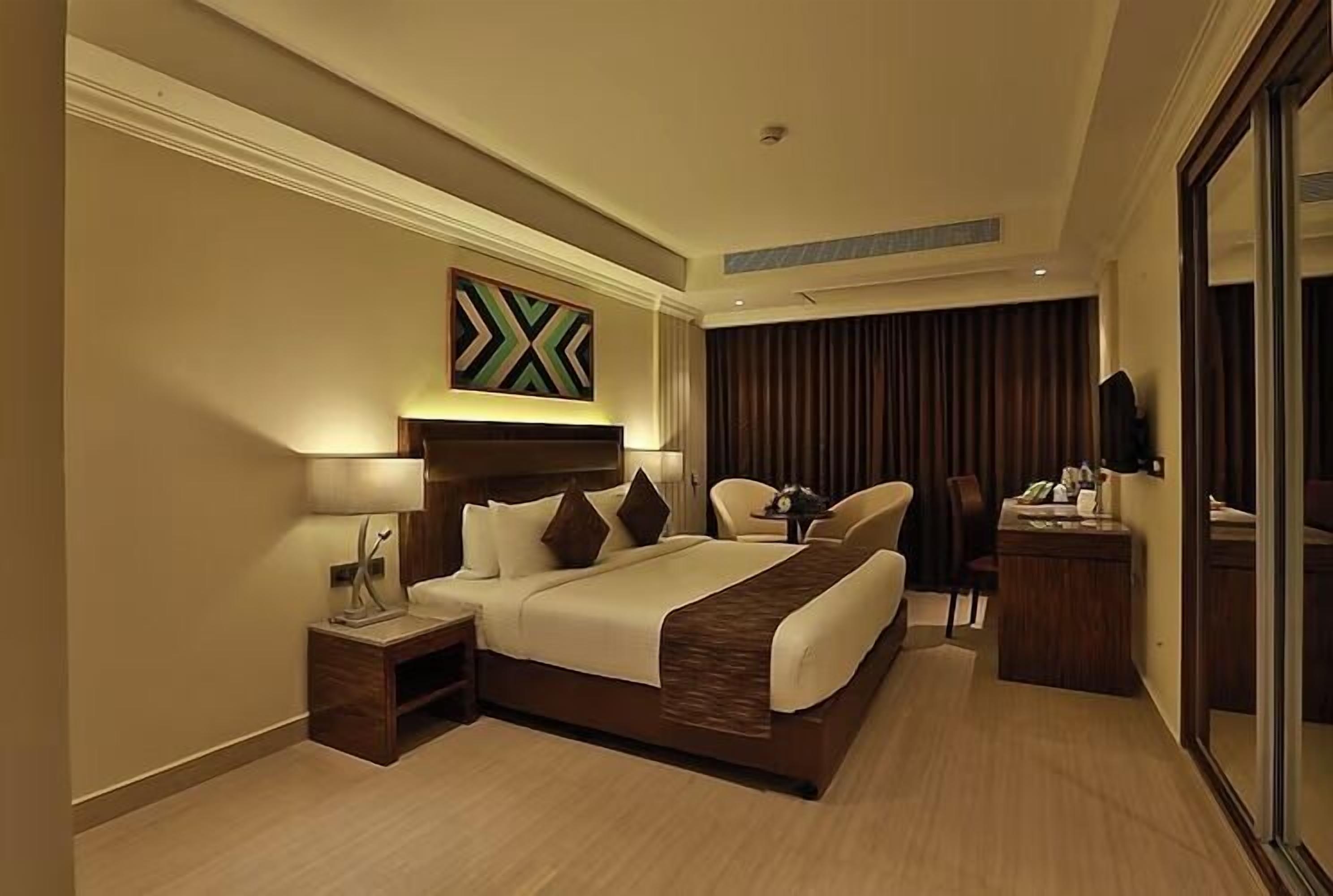 A hotel room with a large bed, bedside table, lamp, and a mirror.
