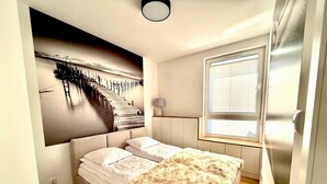 A bedroom with a bed, a large wall mural, a window with blinds, and a door. - Jarzebinowa Loft by JumpInHere (Nowy Dwór Mazowiecki)