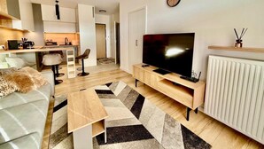 A modern living room with a large flat-screen TV, a sofa, a coffee table, and a kitchen area in the background. - Jarzebinowa Loft by JumpInHere (Nowy Dwór Mazowiecki)