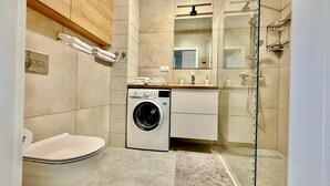 A compact bathroom with a washing machine, toilet, and a glass shower enclosure. - Jarzebinowa Loft by JumpInHere (Nowy Dwór Mazowiecki)