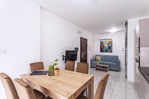 Uma sala de estar moderna com uma mesa de jantar, cadeiras, um sofá, uma televisão e um quadro na parede.