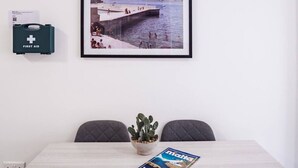 Ein Zimmer mit einem gerahmten Foto von einer Küstenlandschaft, einer Erste-Hilfe-Ausrüstung, einer Kakteenpflanze und einer Zeitschrift auf dem Tisch.