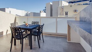 Eine Dachterrasse mit Tisch und Stühlen, einem Blumentopf und Blick auf die umliegenden Gebäude.