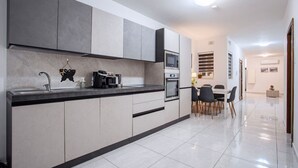 Een moderne keuken met grijze kastjes, een zwart aanrecht en een eethoek met een tafel en stoelen.
