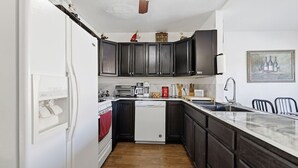 Eine kompakte Küche mit dunklen Schränken, einem weißen Kühlschrank und einem Geschirrspüler.
