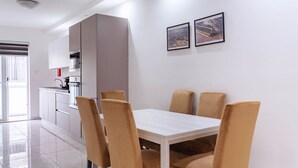 Un comedor moderno con una mesa blanca y cuatro sillas, una cocina con gabinetes blancos y dos cuadros en la pared.