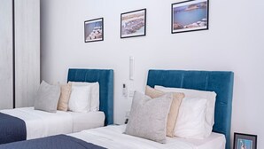 Habitación de hotel con dos camas, cada una con cabecero azul, ropa de cama blanca y varias almohadas. Hay tres cuadros enmarcados en la pared sobre las camas.