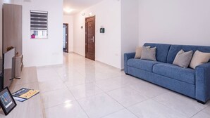 Una sala moderna con un sofá azul, un televisor de pantalla plana y piso de baldosas.
