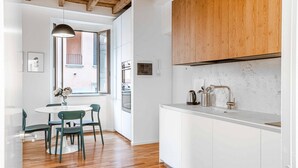 A modern kitchen with white cabinets, a wooden ceiling, and a dining area with a round table and chairs. - Easylife - Milano - Mora 2 - Ticinese  (Milano)
