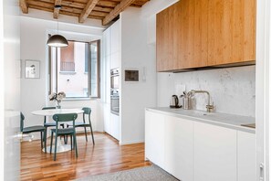 A modern kitchen with white cabinets, a wooden ceiling, and a dining area with a round table and chairs. - Easylife - Milano - Mora 2 - Ticinese  (Milano)