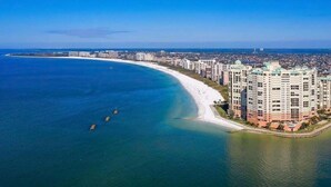 Eine Küstenstadtlandschaft mit einem markanten Hotel direkt am Strand, blauem Himmel und ruhigem Wasser.