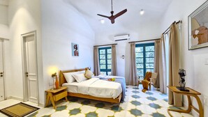 A hotel room with a bed, bedside table, and a chair. There is a window with curtains, a ceiling fan, and a painting on the wall. - Celest 3bhk Villa Siolim Pvt Pool Dancenter (Siolim)
