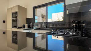 Une cuisine moderne dotée d’un plan de travail noir, d’appareils électroménagers en acier inoxydable et d’une fenêtre offrant une vue sur l’extérieur.