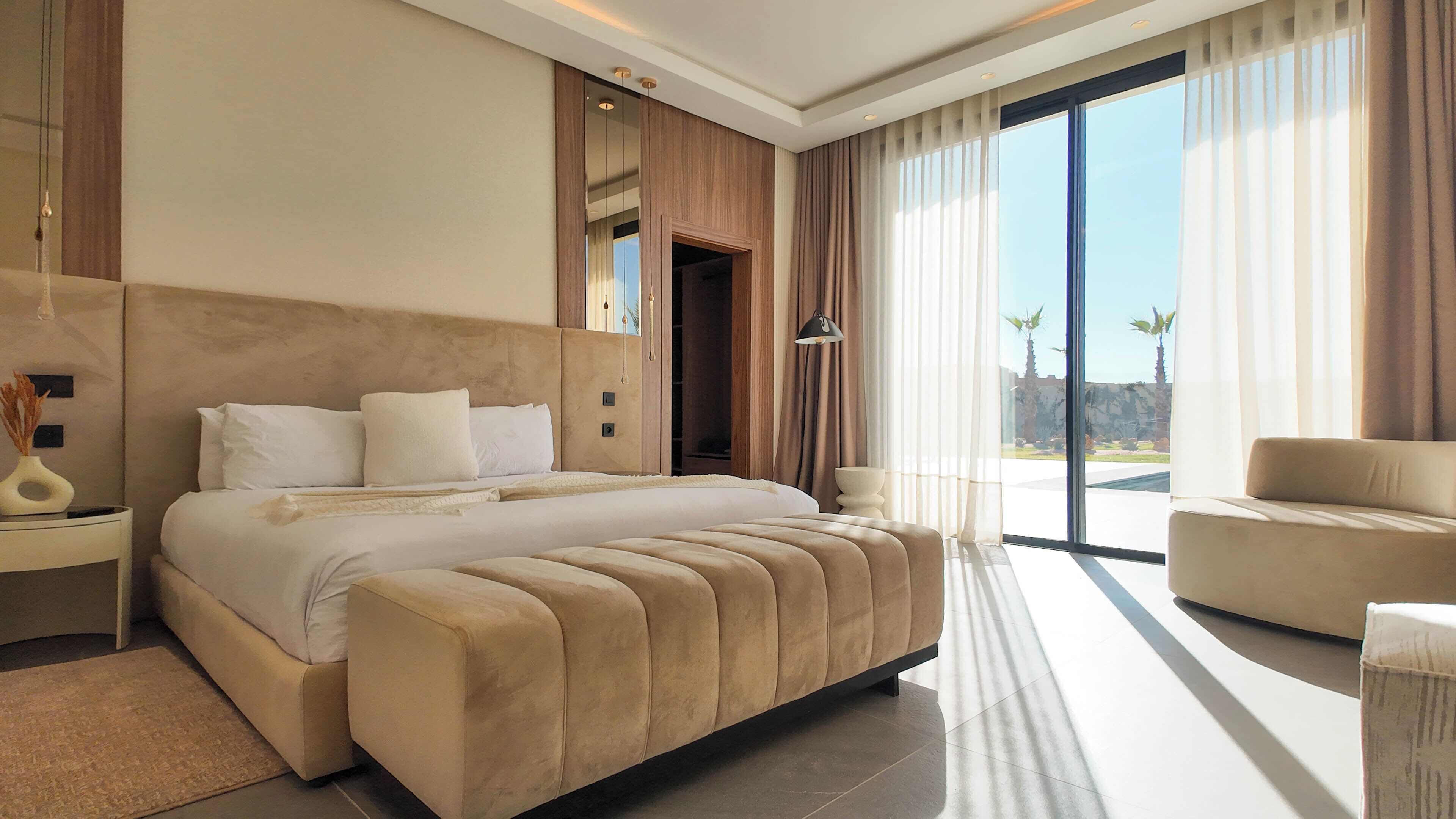 A modern hotel room with a large bed, a seating area, and a view of palm trees.