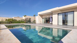 A modern outdoor pool area with a clear pool, a covered seating area, and a building with large windows and a patio. - Villa Janna with a heated pool (Marrakech)