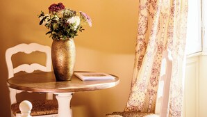 A dining table with a vase of flowers, a chair, a wall-mounted lamp, and a framed picture. - Château de la Grange Moreau - Pierre Moreau room (Vallon-sur-Gée)
