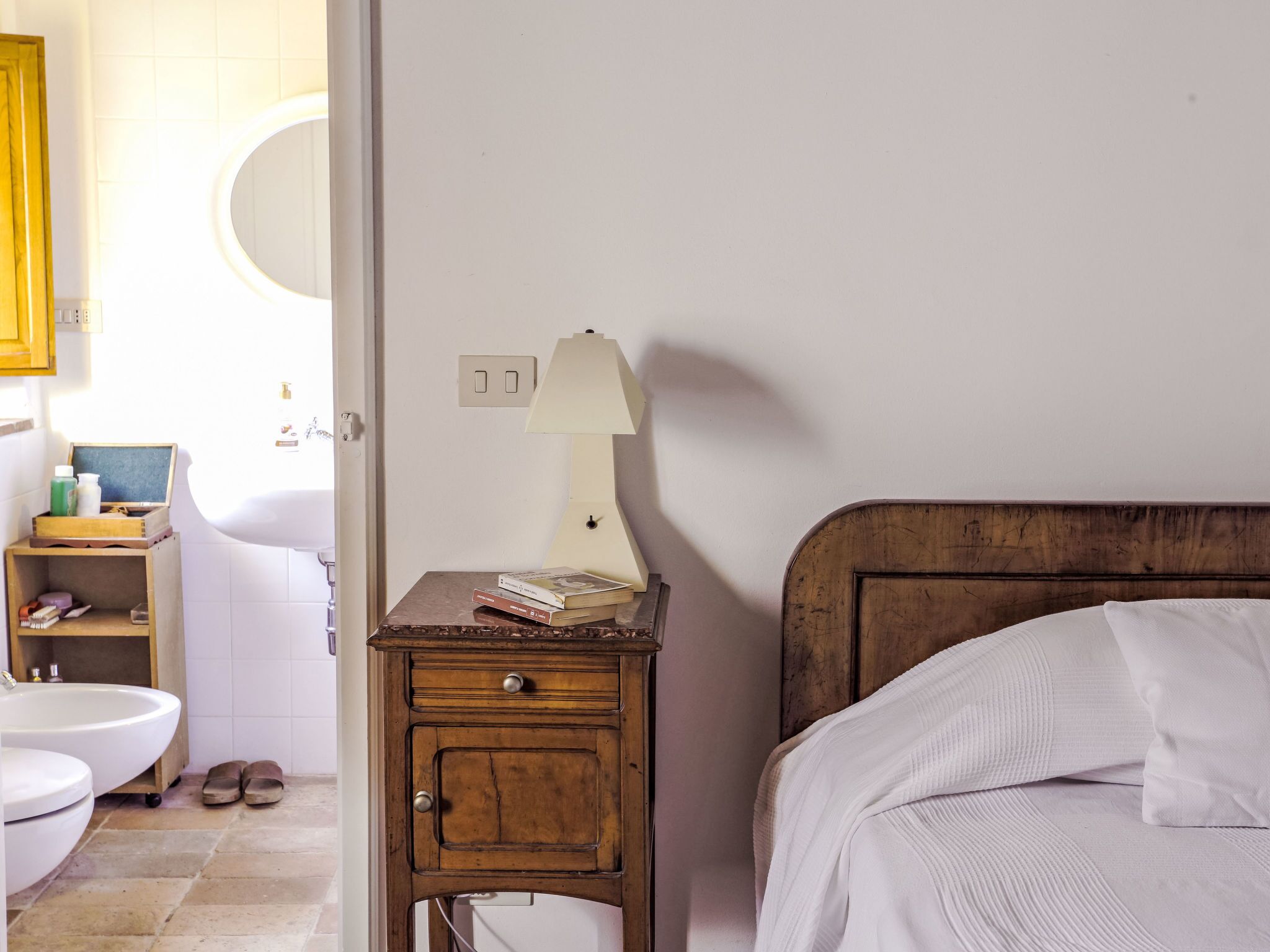Une chambre à coucher avec une table de chevet en bois, une lampe blanche, un lit avec une literie blanche et une tête de lit en bois.