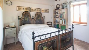 A bedroom with a bed, a bedside table, a clock, framed pictures, a bookshelf, and a window.