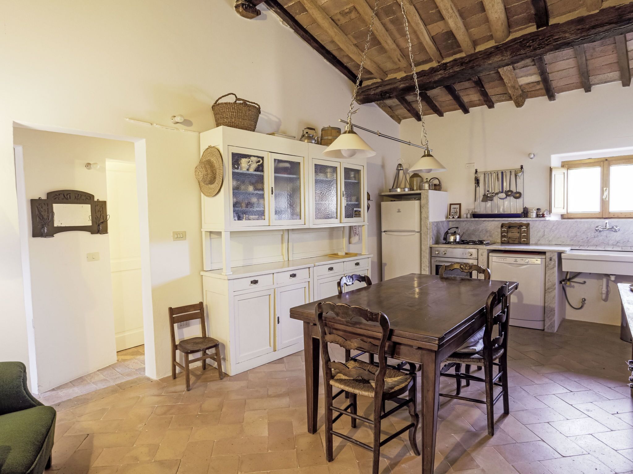 A kitchen with a wooden table and chairs, a refrigerator, and a window with wooden shutters.