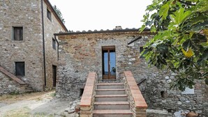 A stone staircase leading to a wooden door, with a rustic stone building on one side and a tree with broad leaves on the other.
