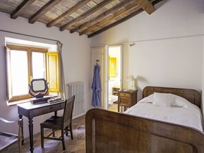 Une chambre à coucher avec un lit en bois, un bureau avec une chaise, une fenêtre et une salle de bain visible à travers une porte ouverte.