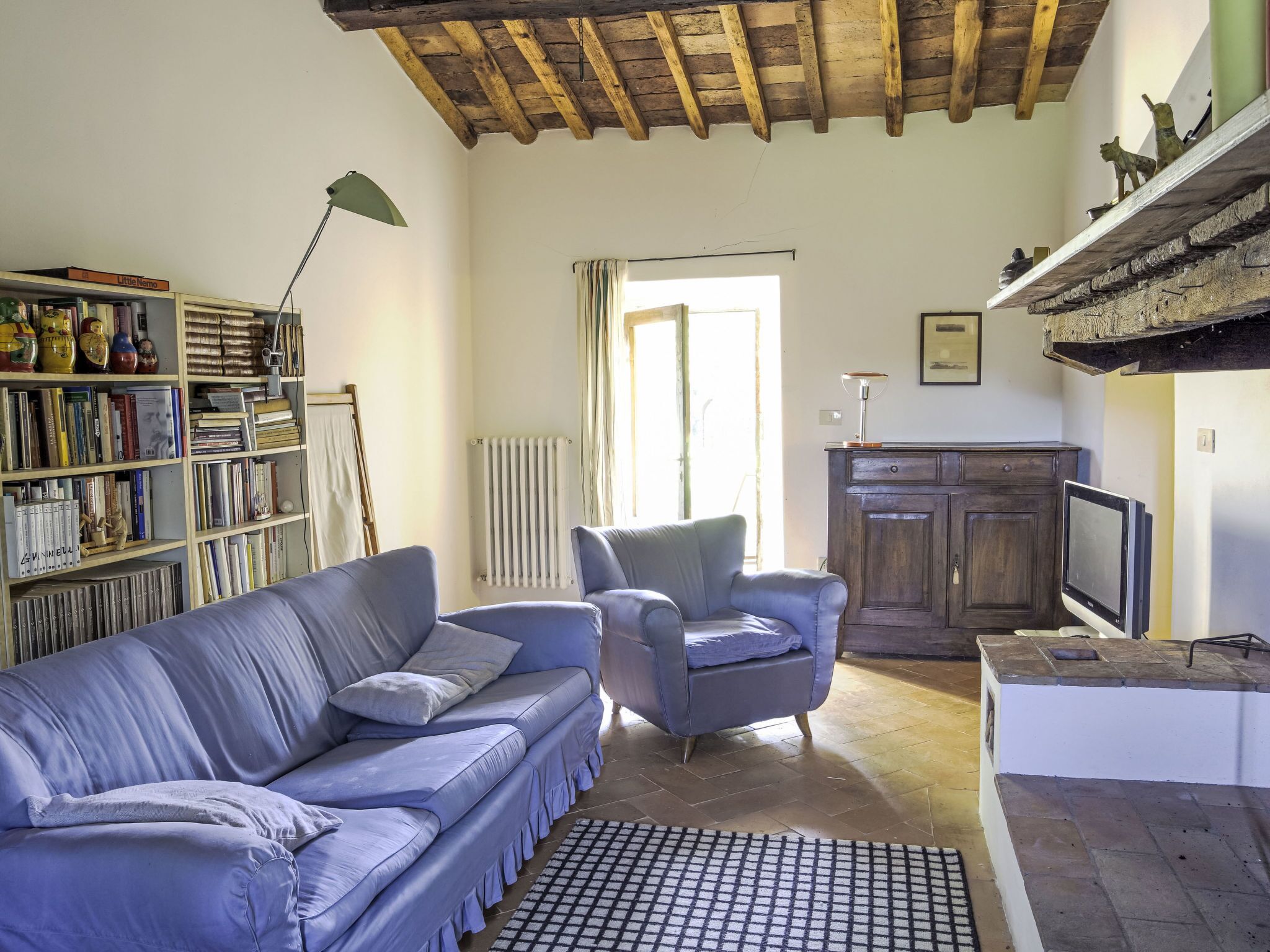 Un salon comprenant un canapé, un fauteuil et une bibliothèque remplie de livres et d’objets décoratifs.