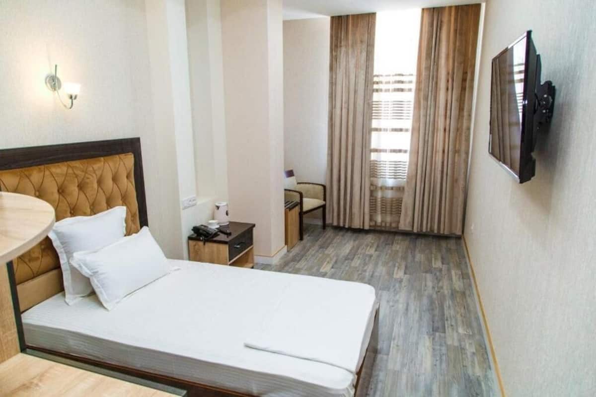 Ein Hotelzimmer mit Bett, Nachttisch, Lampe und einem an der Wand befestigten Fernseher.