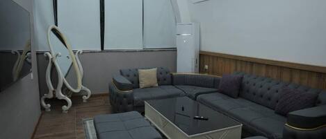 A modern living room with a sectional sofa, ottomans, a glass coffee table, and a large mirror.