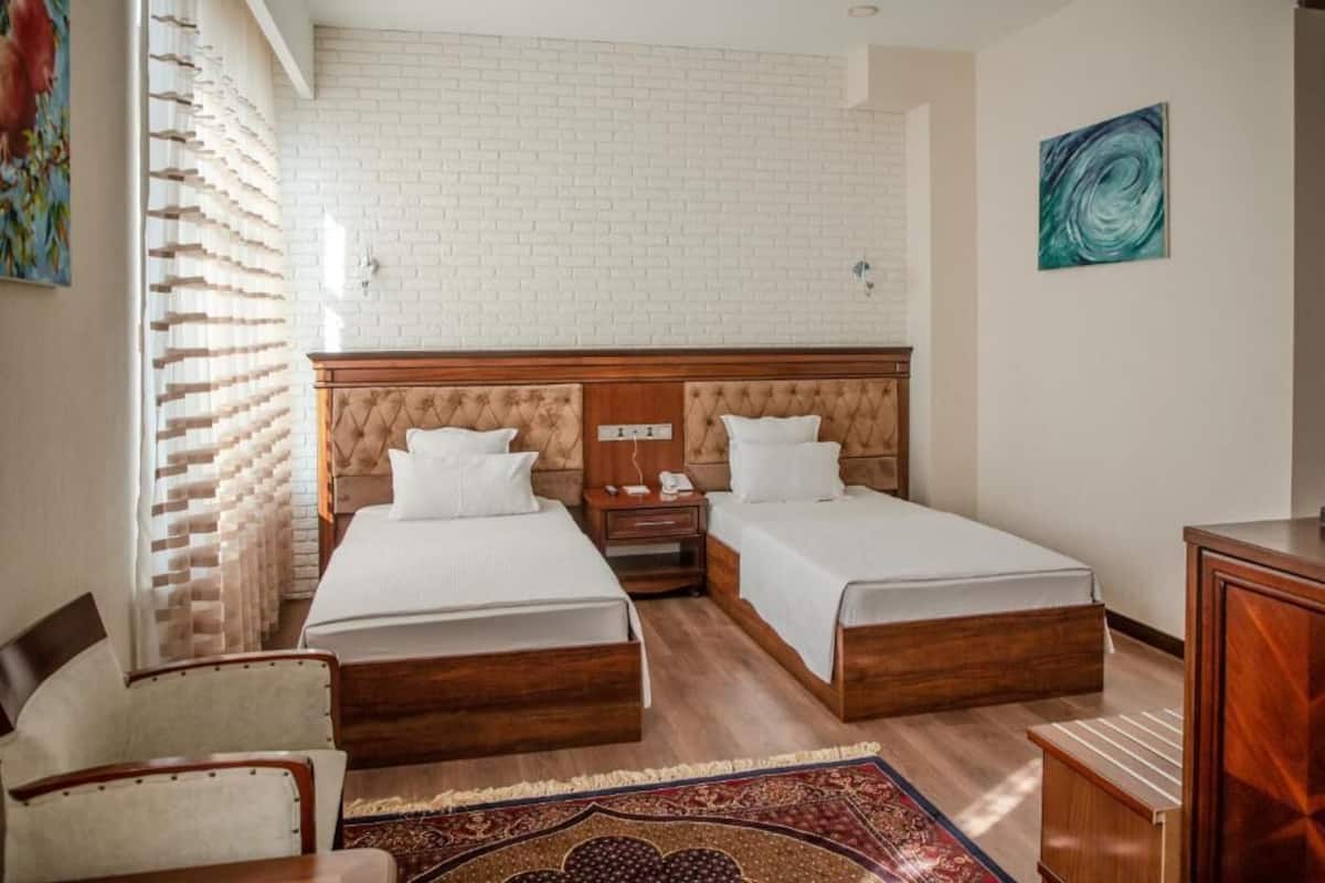 Ein Hotelzimmer mit zwei Betten, einem Holzkopfende, einem Nachttisch, einem Schreibtisch und einem gemusterten Teppich.