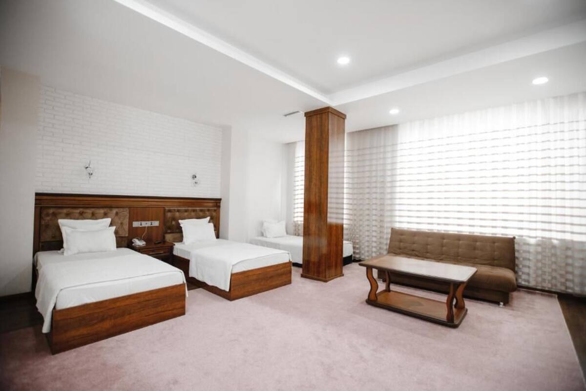 Ein Hotelzimmer mit zwei Betten, einem Schlafsofa, einem Holztisch und einem großen Fenster mit Jalousien.