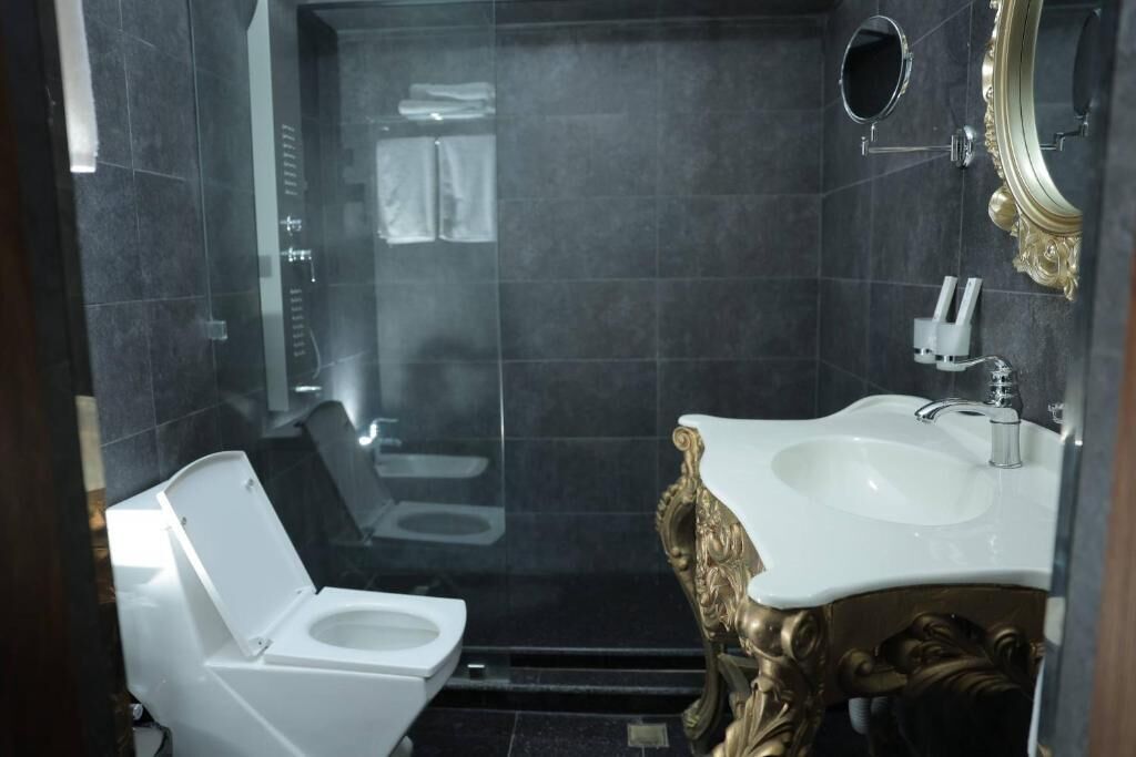 A compact bathroom with a white toilet, a sink with a gold ornate base, and a mirror with a gold frame.