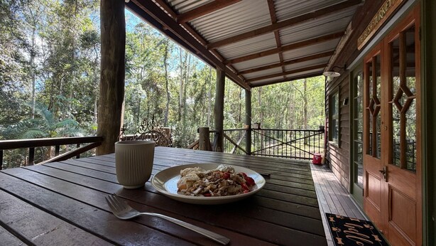 A wooden deck with a table, a plate of food, and a fork. - Mary River Hideaway - Bush Turkey Retreat a place to unwind surrounded by nature (Conondale)