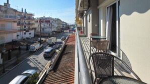 A balcony with wicker chairs, a view of a street with parked cars, and buildings in the background.