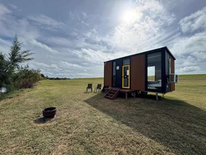 Een moderne, gelijkvloerse hut met een grote glazen deur, een klein terras en uitzicht op een grasveld.