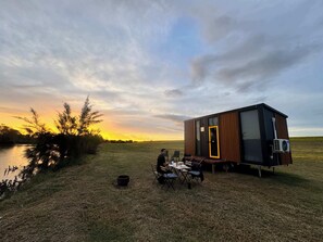 Een klein huisje met een deur, een tafel met stoelen en een zittende persoon.
