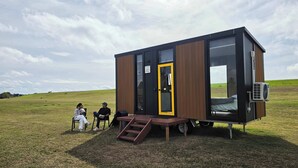 A modern, compact cabin with a large sliding door, a small outdoor seating area, and a bed visible through the window.