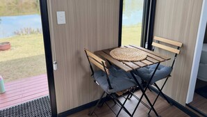Huone, josta on näkymä järvelle, pöytä, jonka päällä on kudottu alusta, pehmusteella varustettu tuoli ja puinen penkki.