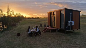 A modern, compact cabin with a sliding door, a small deck, and a portable air conditioning unit.