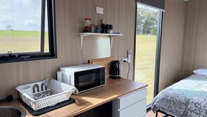 A modern room with a wooden desk, a microwave, a coffee maker, a basket, and a bed with a patterned bedspread.