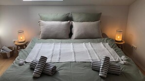 Una camera da letto con un lucernario, due abat-jour, un letto con biancheria verde e asciugamani a righe.