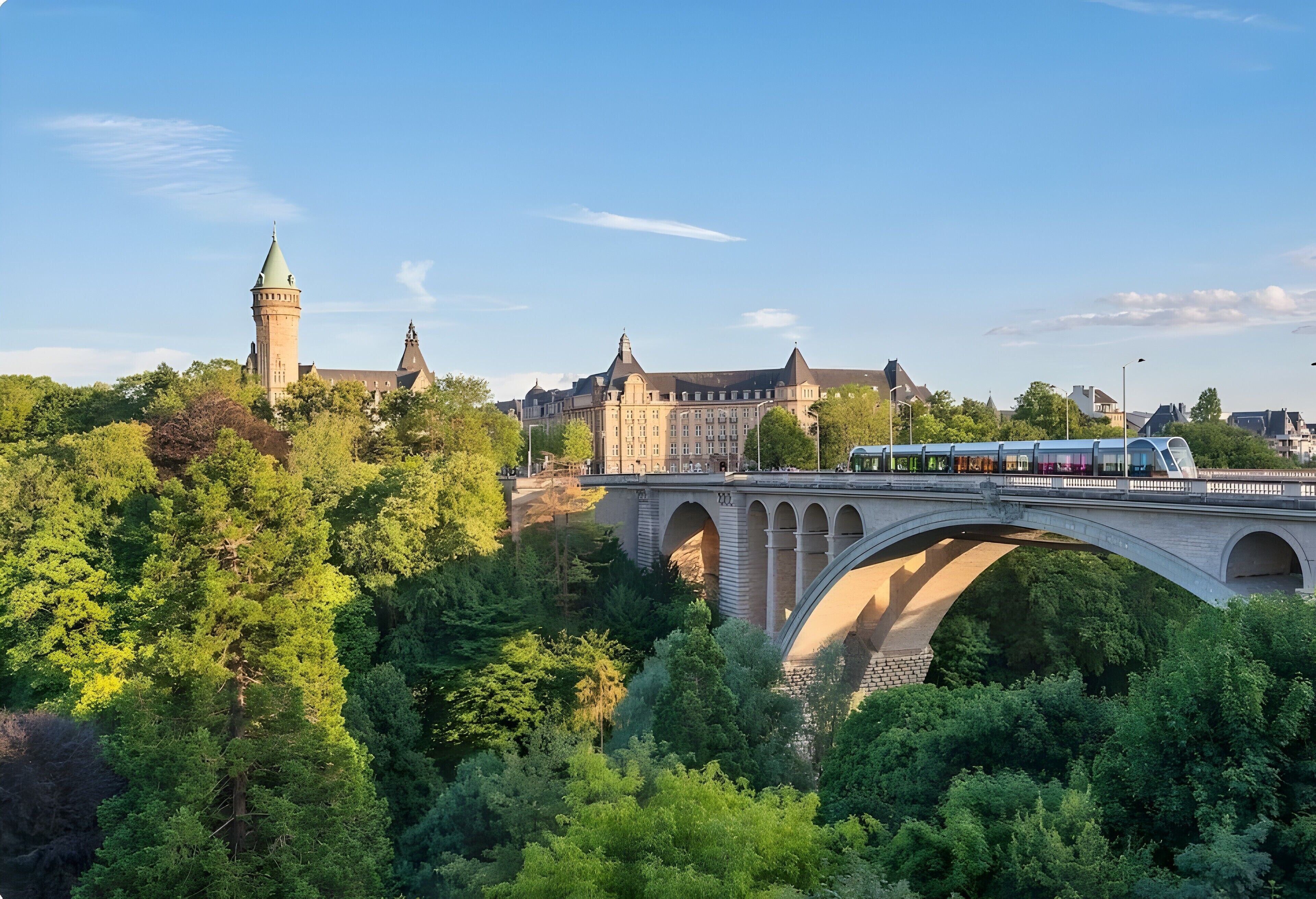 A bridge with a train, a historic building, and dense greenery.