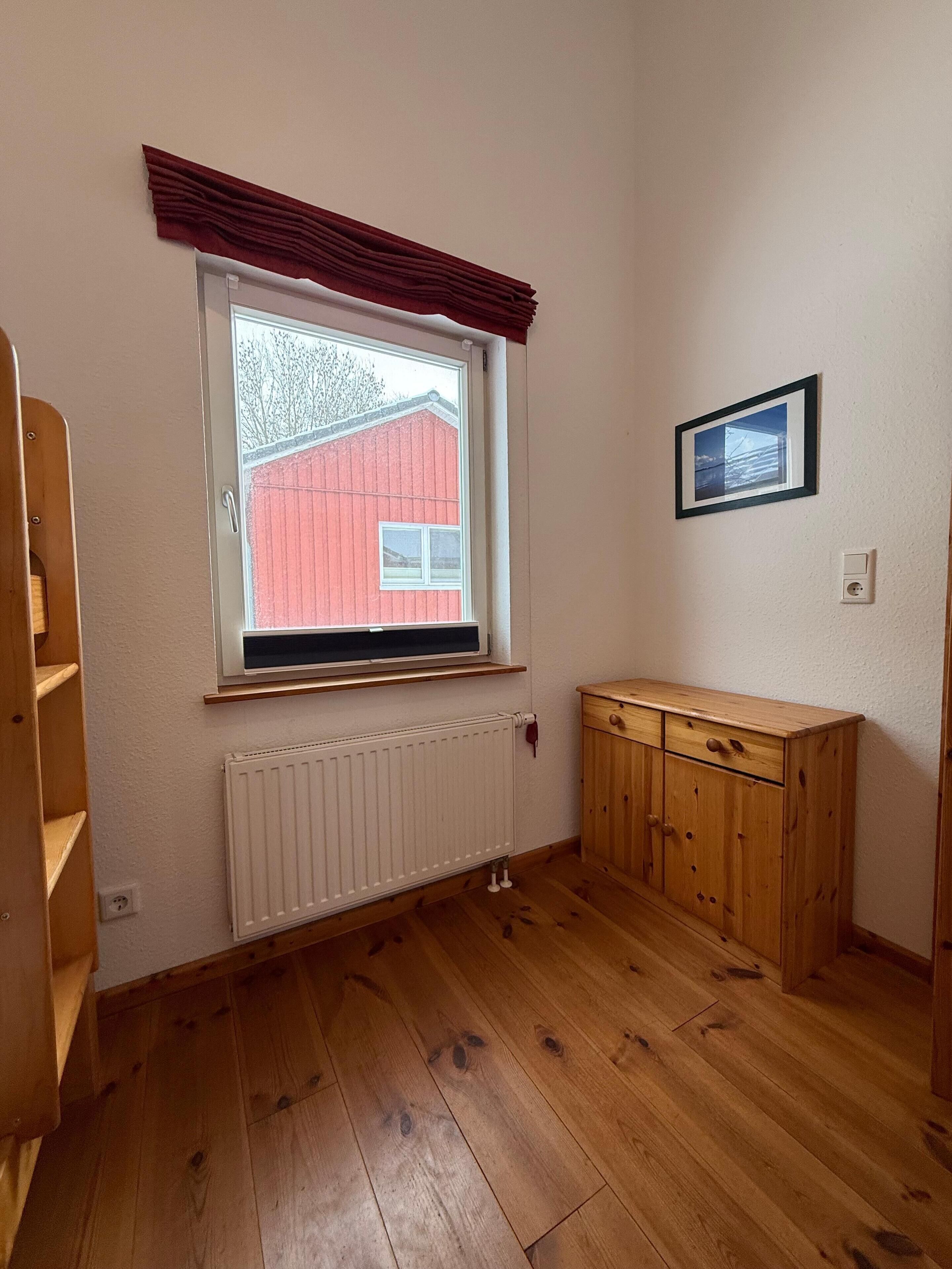 A room with a window, wooden floor, radiator, and a wooden cabinet.
